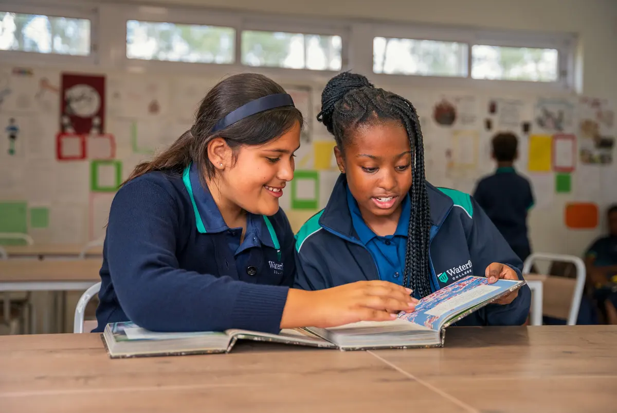 Two students reading a book together at a classroom desk